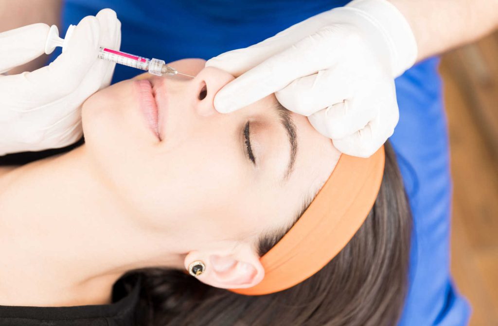 An expert dermatologist performing a non-surgical rhinoplasty treatment on a female patient using injectable fillers.