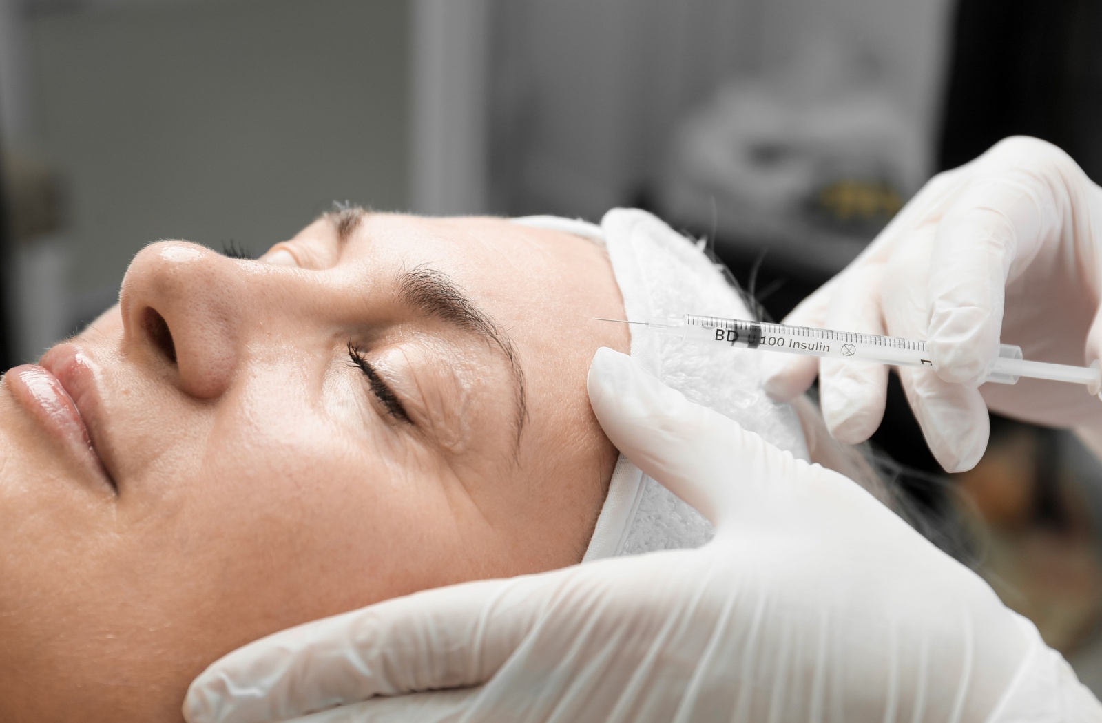 A close-up of a woman getting botox injected into her forehead.