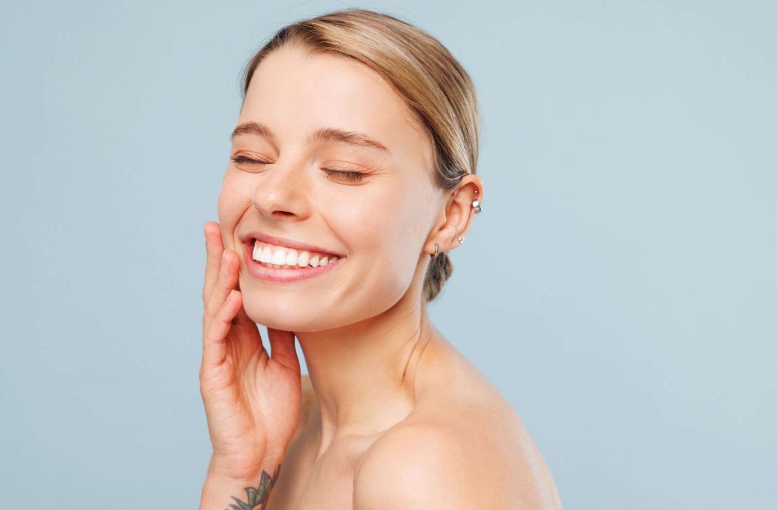 A patient smiling and feeling their cheek after Botox treatment against a blue background.