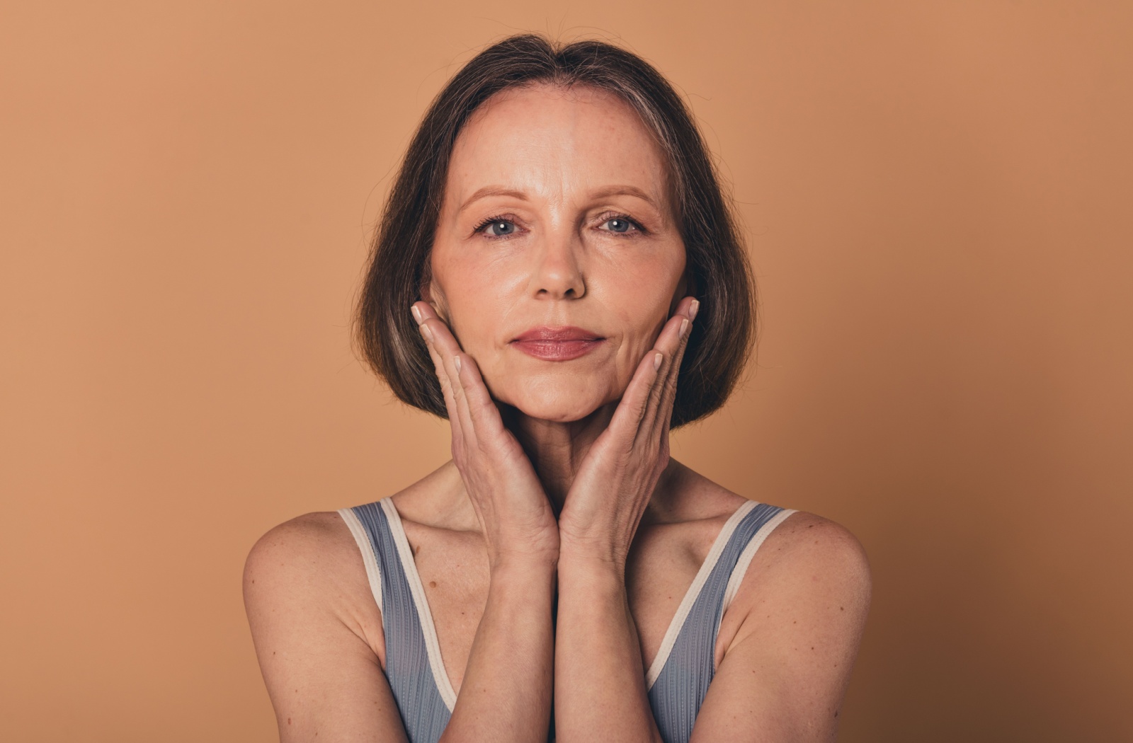 A person with mature skin caressing their face, showcasing their lifted and youthful-looking features.
